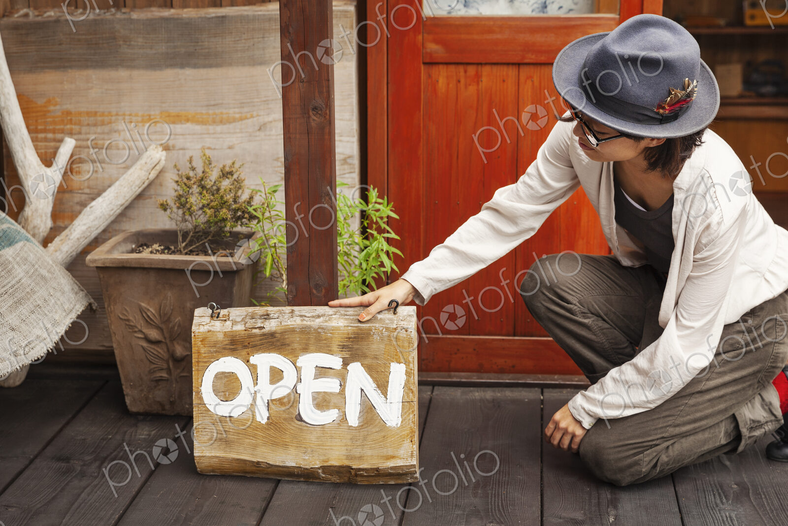 Japanese woman wearing hat and glasses kneeling in front of a leather shop, holding…