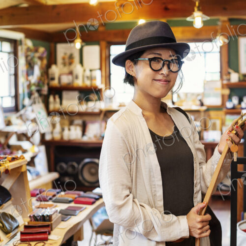 Japanese woman wearing hat and glasses standing in a leather shop, holding leather belt.