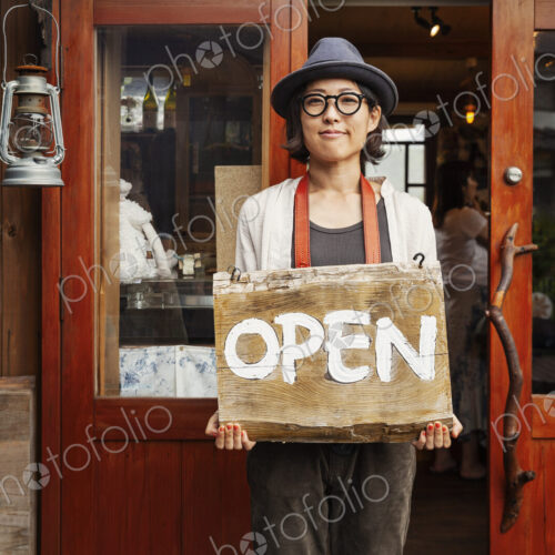 Japanese woman wearing hat and glasses standing in front of a leather shop, holding…