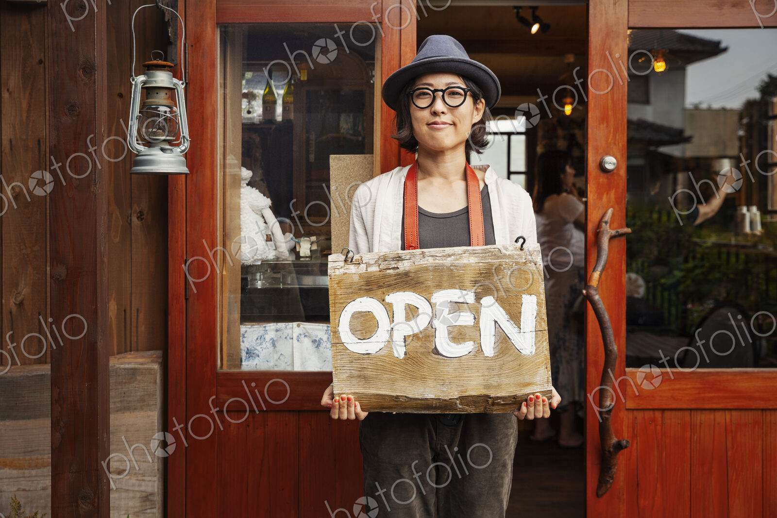 Japanese woman wearing hat and glasses standing in front of a leather shop, holding…