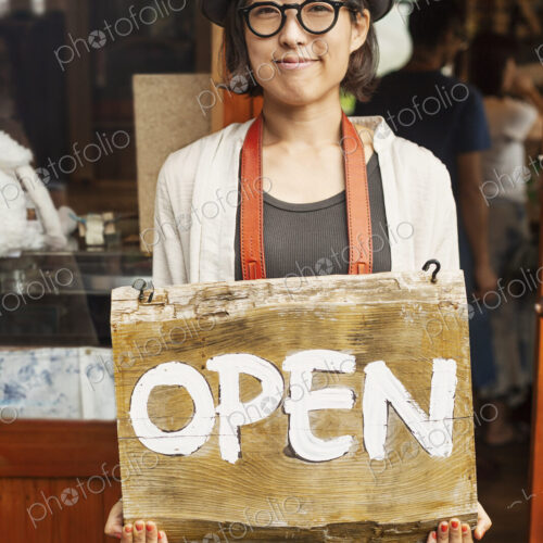 Japanese woman wearing hat and glasses standing in front of a leather shop, holding…