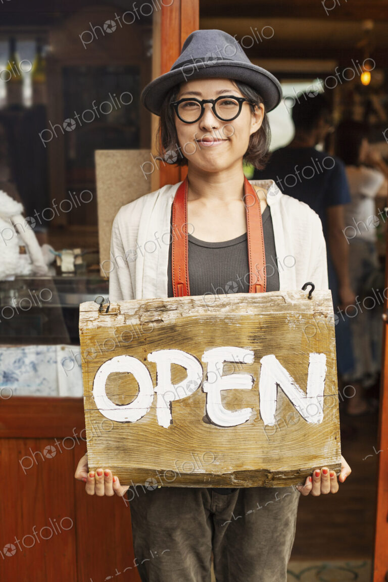 Japanese woman wearing hat and glasses standing in front of a leather shop, holding…