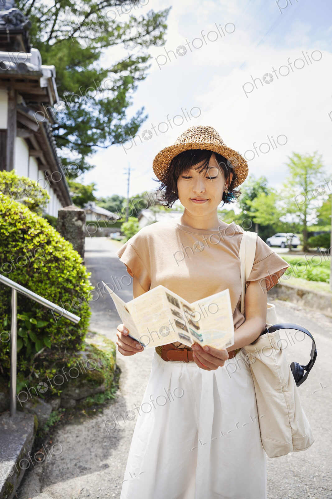 Japanese woman wearing hat and holding map standing outside Buddhist temple.