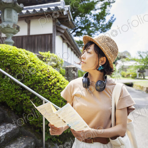 Japanese woman wearing hat and holding map standing outside Buddhist temple. Japanese woman wearing hat and holding map standing outside Buddhist temple.