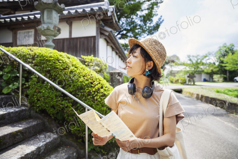 Japanese woman wearing hat and holding map standing outside Buddhist temple.