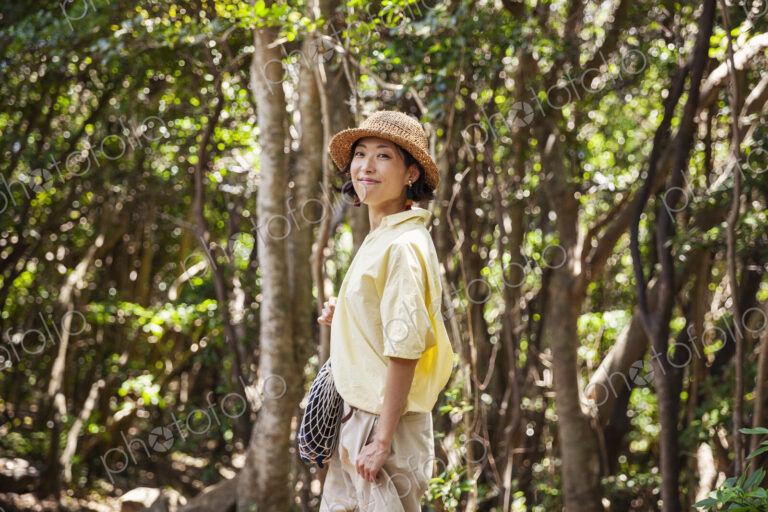 Japanese woman wearing hat hiking in a forest.
