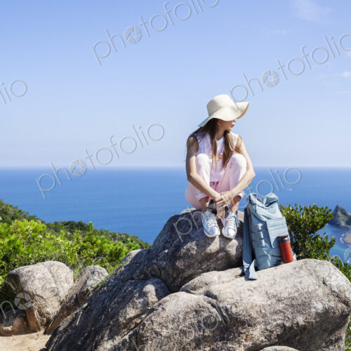 Japanese woman wearing hat sitting on rock on a cliff, ocean in the background. Japanese woman wearing hat sitting on rock on a cliff, ocean in the background.