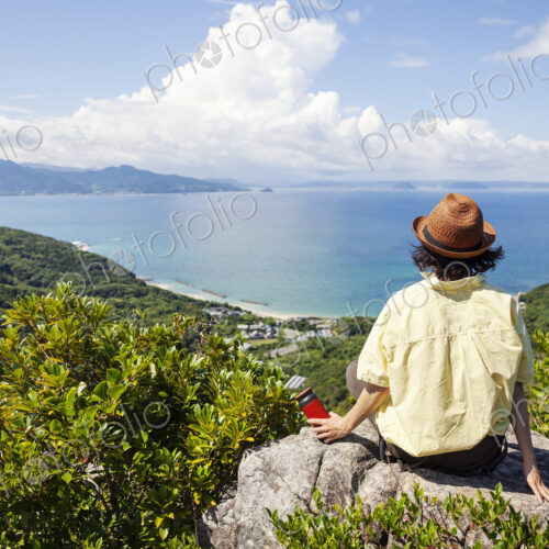 Japanese woman wearing hat sitting on rock on a cliff, ocean in the background. Japanese woman wearing hat sitting on rock on a cliff, ocean in the background.