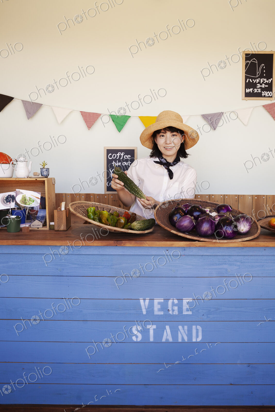 Japanese woman wearing hat standing behind counter in a farm shop, smiling at camera.
