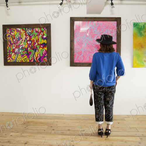 Japanese woman wearing hat standing in front of abstract painting in an art gallery.