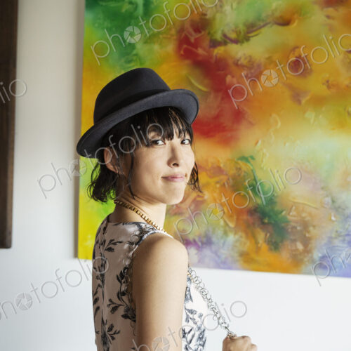Japanese woman wearing hat standing in front of abstract painting in an art gallery.