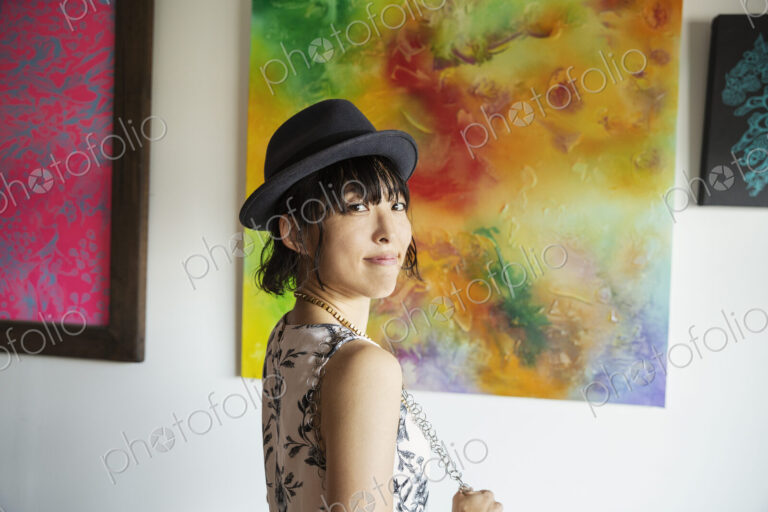 Japanese woman wearing hat standing in front of abstract painting in an art gallery.