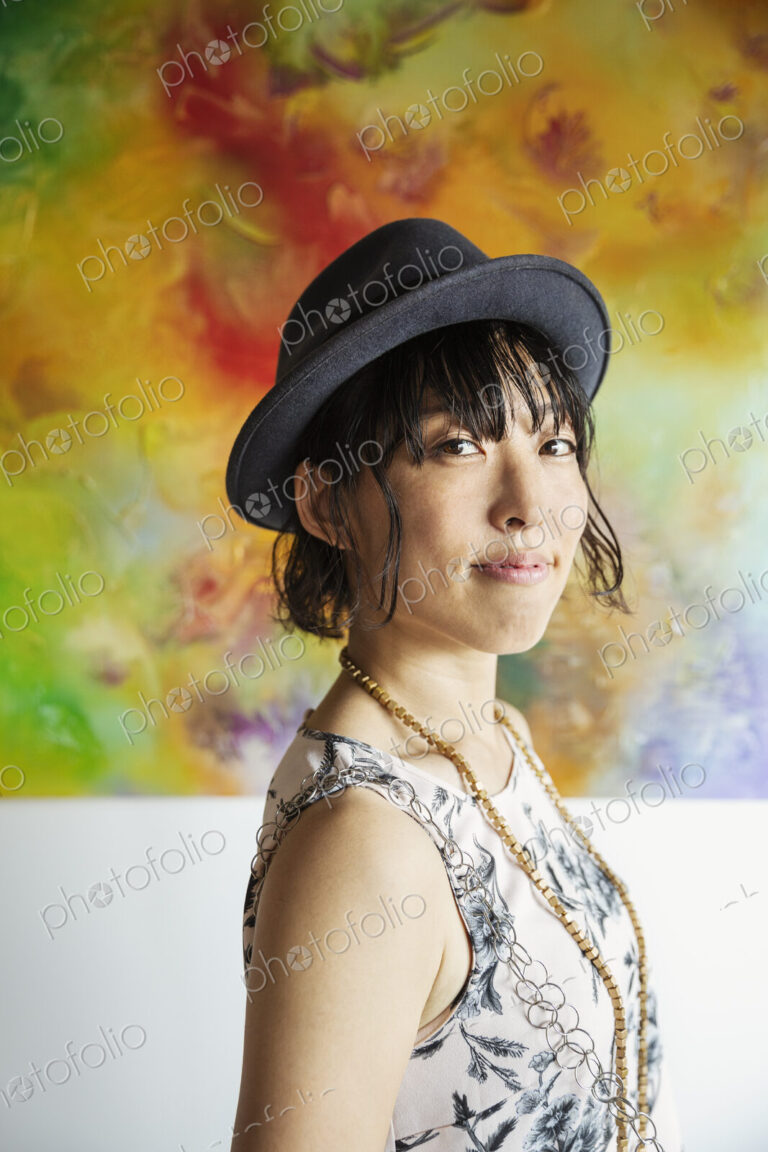 Japanese woman wearing hat standing in front of abstract painting in an art gallery.