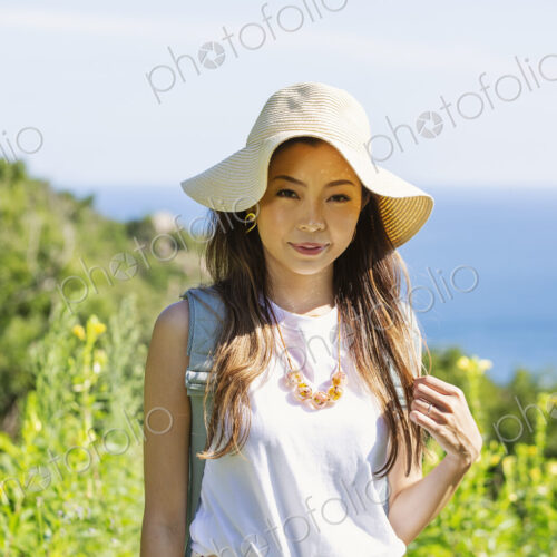 Japanese woman wearing hat standing on a cliff, ocean in the background.