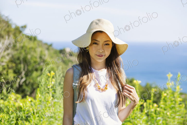 Japanese woman wearing hat standing on a cliff, ocean in the background.