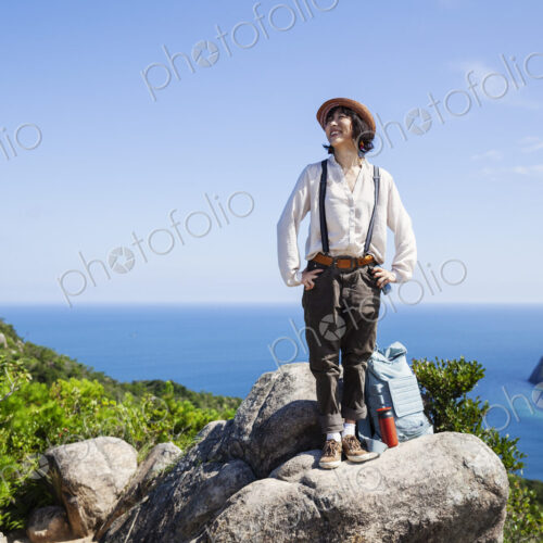 Japanese woman wearing hat standing on a rock on cliff, ocean in the background. Japanese woman wearing hat standing on a rock on cliff, ocean in the background.