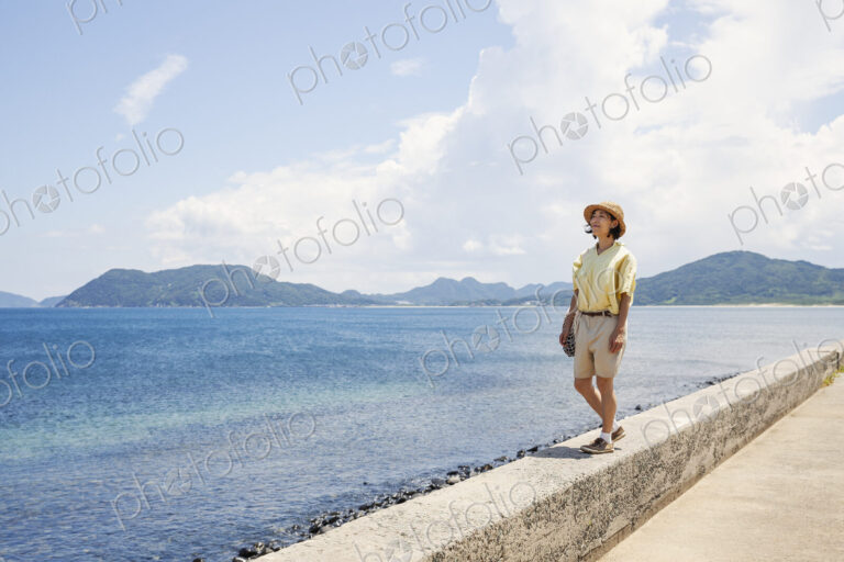 Japanese woman wearing hat standing on a wall, looking at ocean.