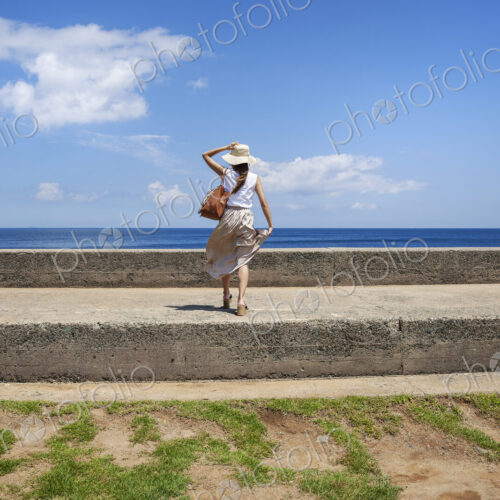 Japanese woman wearing hat standing on a wall, ocean in the background. Japanese woman wearing hat standing on a wall, ocean in the background.