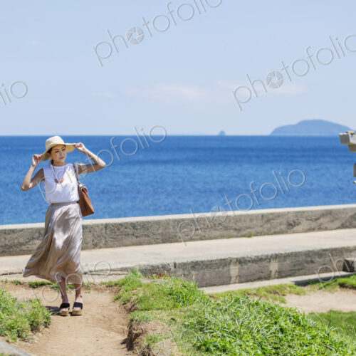 Japanese woman wearing hat walking along path by the ocean. Japanese woman wearing hat walking along path by the ocean.