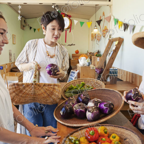 Japanese woman wearing hat working in a farm shop, serving two female customers. Japanese woman wearing hat working in a farm shop, serving two female customers.