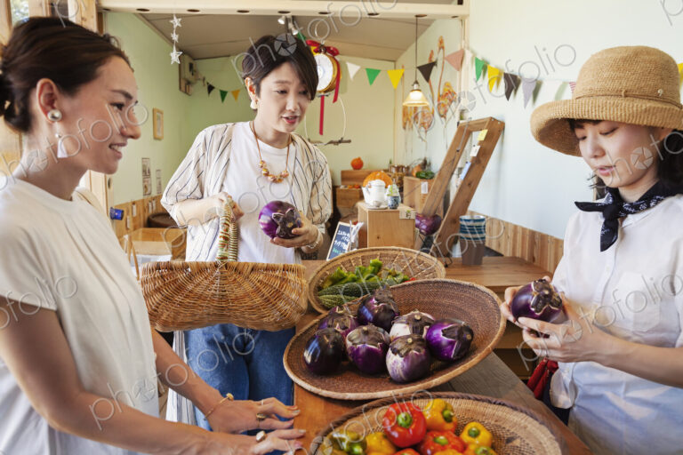 Japanese woman wearing hat working in a farm shop, serving two female customers.