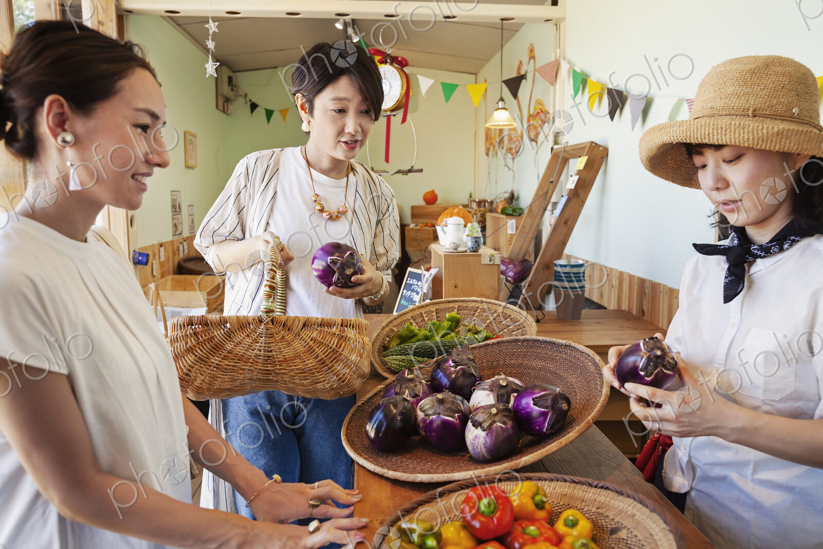 Japanese woman wearing hat working in a farm shop, serving two female customers.