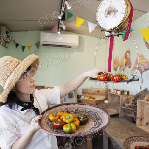 Japanese woman wearing hat working in a farm shop, weighing fresh vegetables.