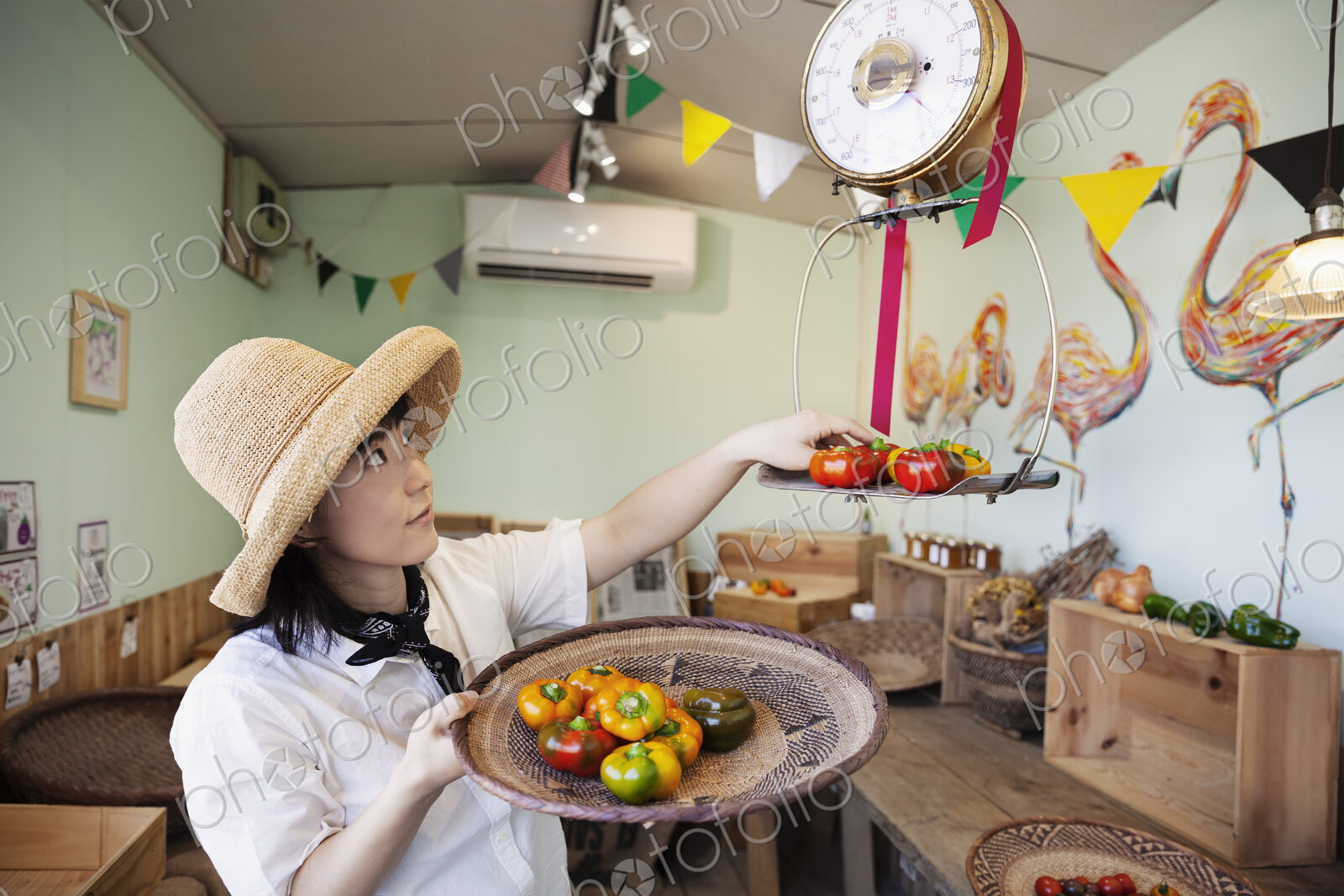 Japanese woman wearing hat working in a farm shop, weighing fresh vegetables.