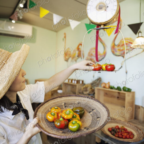 Japanese woman wearing hat working in a farm shop, weighing fresh vegetables.