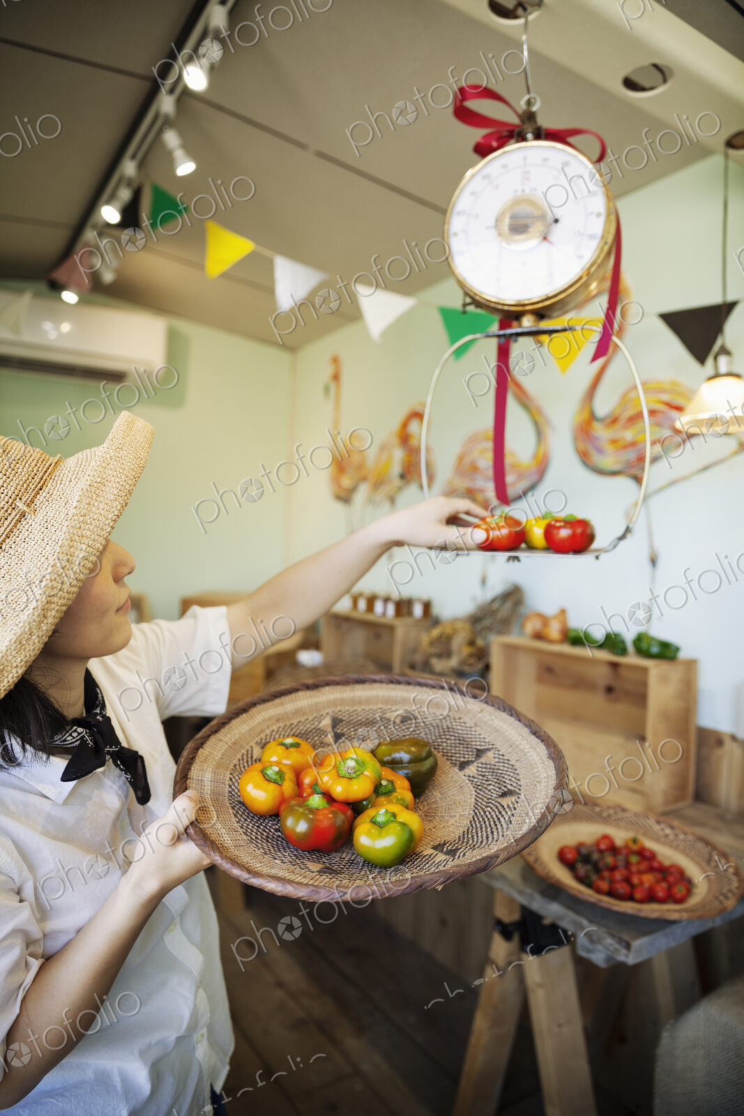 Japanese woman wearing hat working in a farm shop, weighing fresh vegetables.
