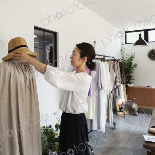 Japanese women standing in a small fashion boutique, arranging hat on mannequin. Japanese women standing in a small fashion boutique, arranging hat on mannequin.