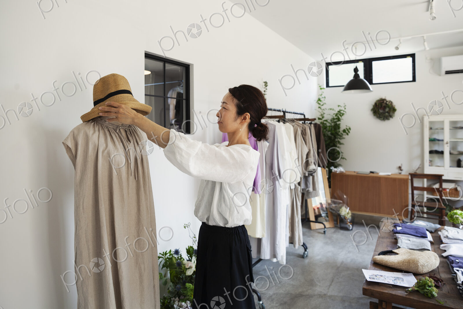 Japanese women standing in a small fashion boutique, arranging hat on mannequin.