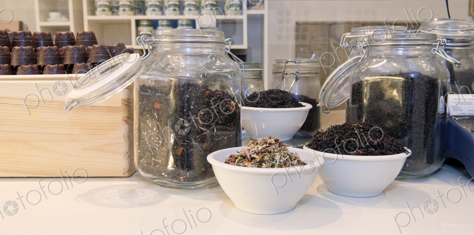 Jars and cups filled with various blends of tea on the counter of a lunchroom.