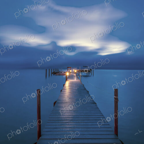 Jetty dock onto ocean at dawn with dramatic sky above.