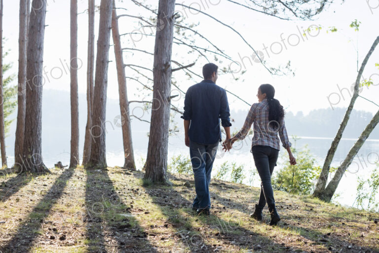 Lakeside. A couple walking in the shade of pine trees in summer.