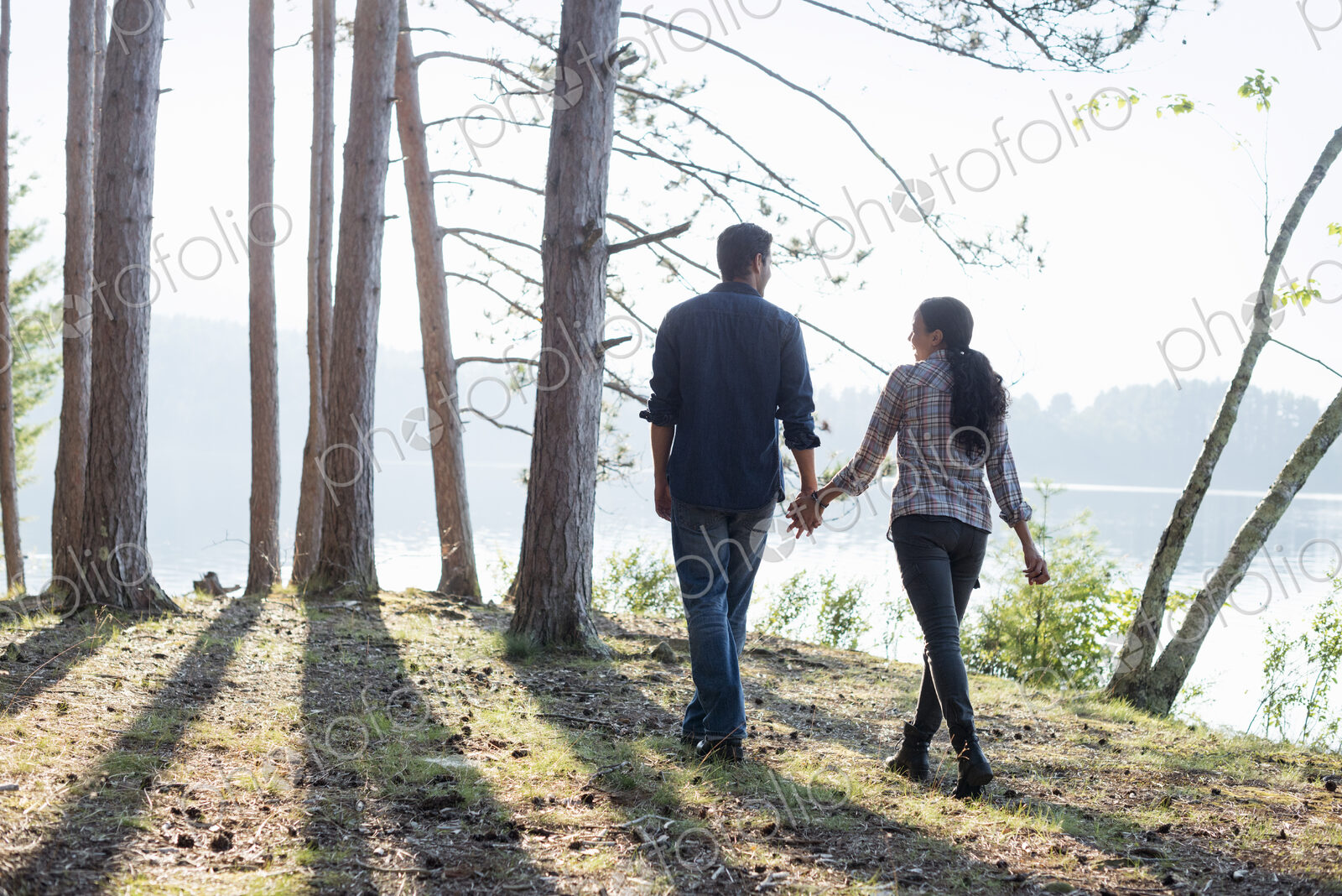Lakeside. A couple walking in the shade of pine trees in summer.