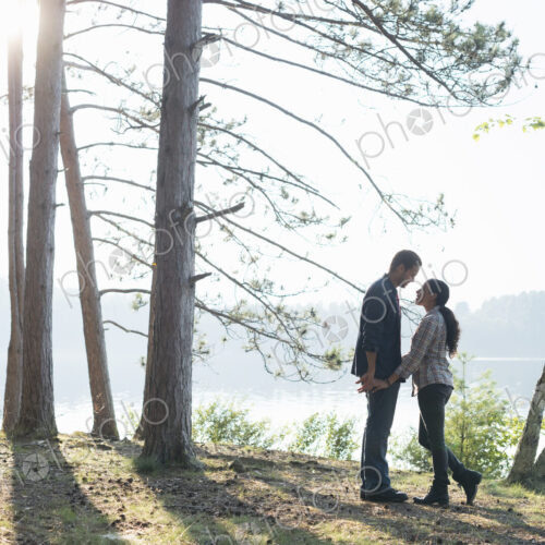 Lakeside. A couple walking in the shade of pine trees in summer. Lakeside. A couple walking in the shade of pine trees in summer.