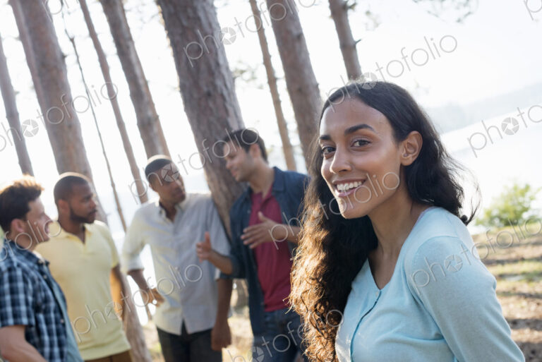 Lakeside. A group of people, friends gathered in the shade of pine trees in summer.