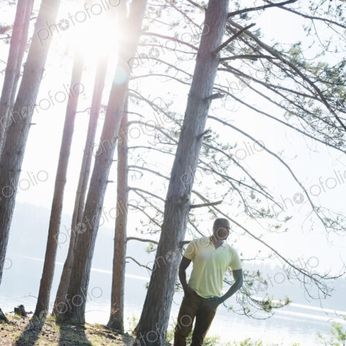 Lakeside. A man standing in the shade of pine trees in summer. Lakeside. A man standing in the shade of pine trees in summer.