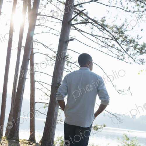 Lakeside. A man standing in the shade of pine trees in summer. Lakeside. A man standing in the shade of pine trees in summer.