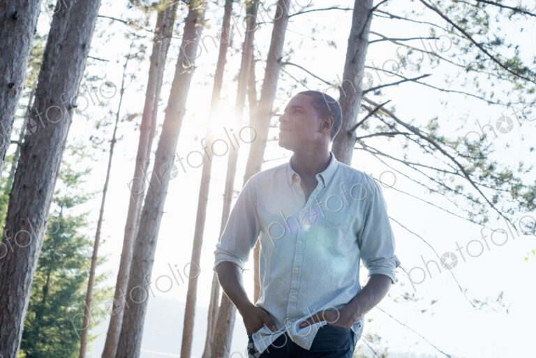 Lakeside. A man standing in the shade of pine trees in summer.