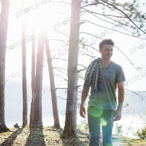 Lakeside. A man standing in the shade of pine trees in summer. Lakeside. A man standing in the shade of pine trees in summer.