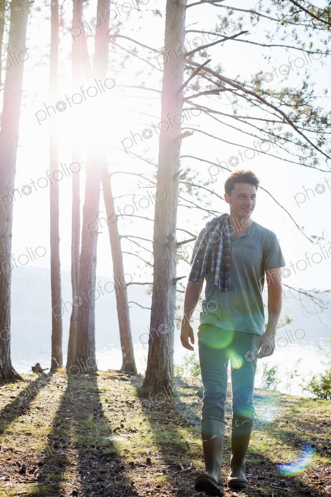 Lakeside. A man standing in the shade of pine trees in summer.