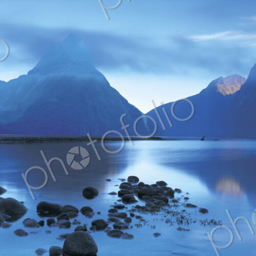 Landscape with lake surrounded by mountains at dusk.