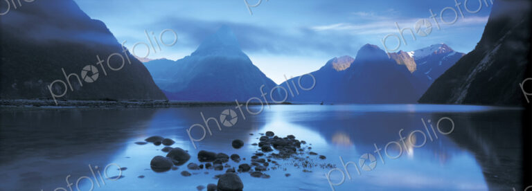 Landscape with lake surrounded by mountains at dusk.