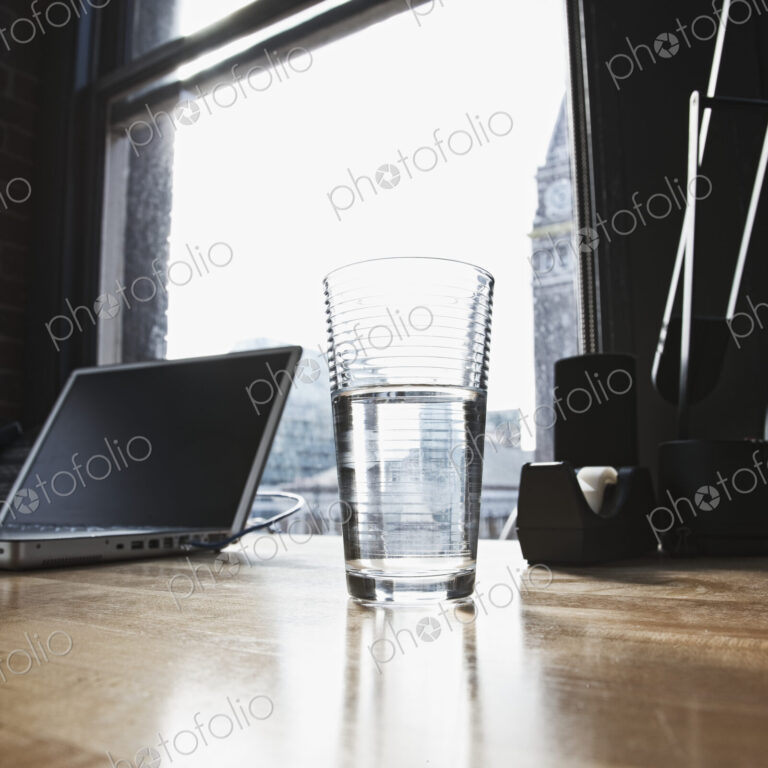 Laptop and drinking water glass on desk in urban office.