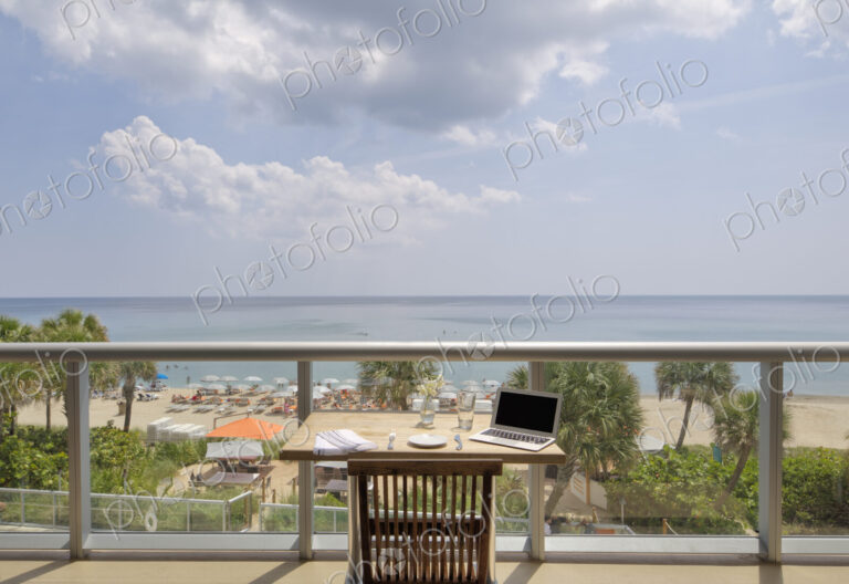 Laptop on restaurant balcony table overlooking beach