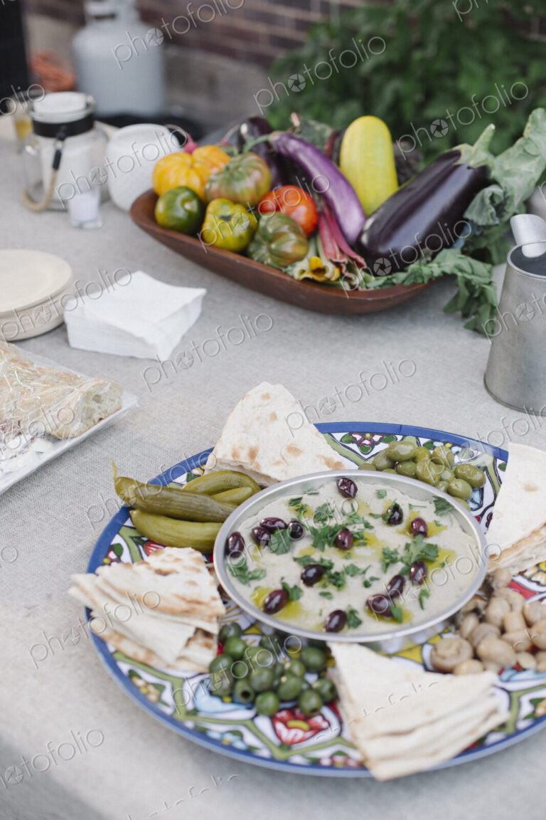 Large bowl of vegetables, dips and bread on a table in a garden.