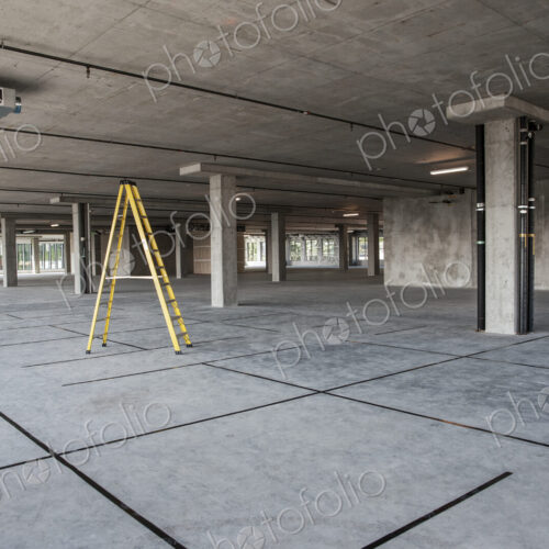 Large empty raw office space with a ladder set up on the floor.
