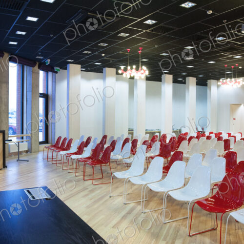 Large empty room with red and white chairs in rows, ready for a presentation Large empty room with red and white chairs in rows, ready for a presentation